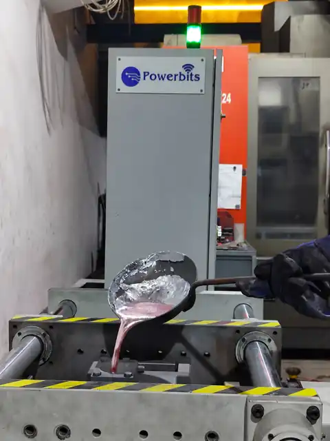 Molten metal being poured into a die on a Powerbits machine, with the Powerbits control cabinet visible